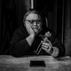 Guillermo del Toro, in a black sweater, stares enigmatically at a model of Pinocchio.